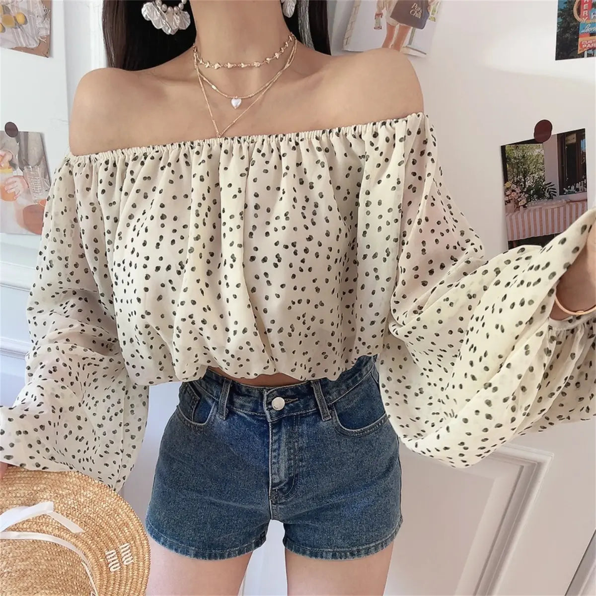 Front view of the off-shoulder cream blouse with black dot print, styled with layered gold necklaces and denim shorts