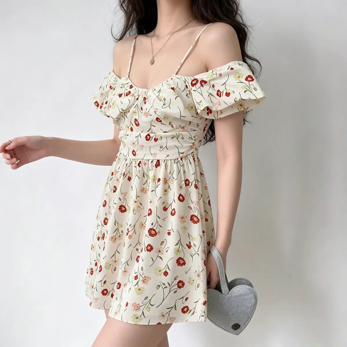 Model wearing an off-shoulder floral mini dress with spaghetti straps, holding a heart-shaped bag.