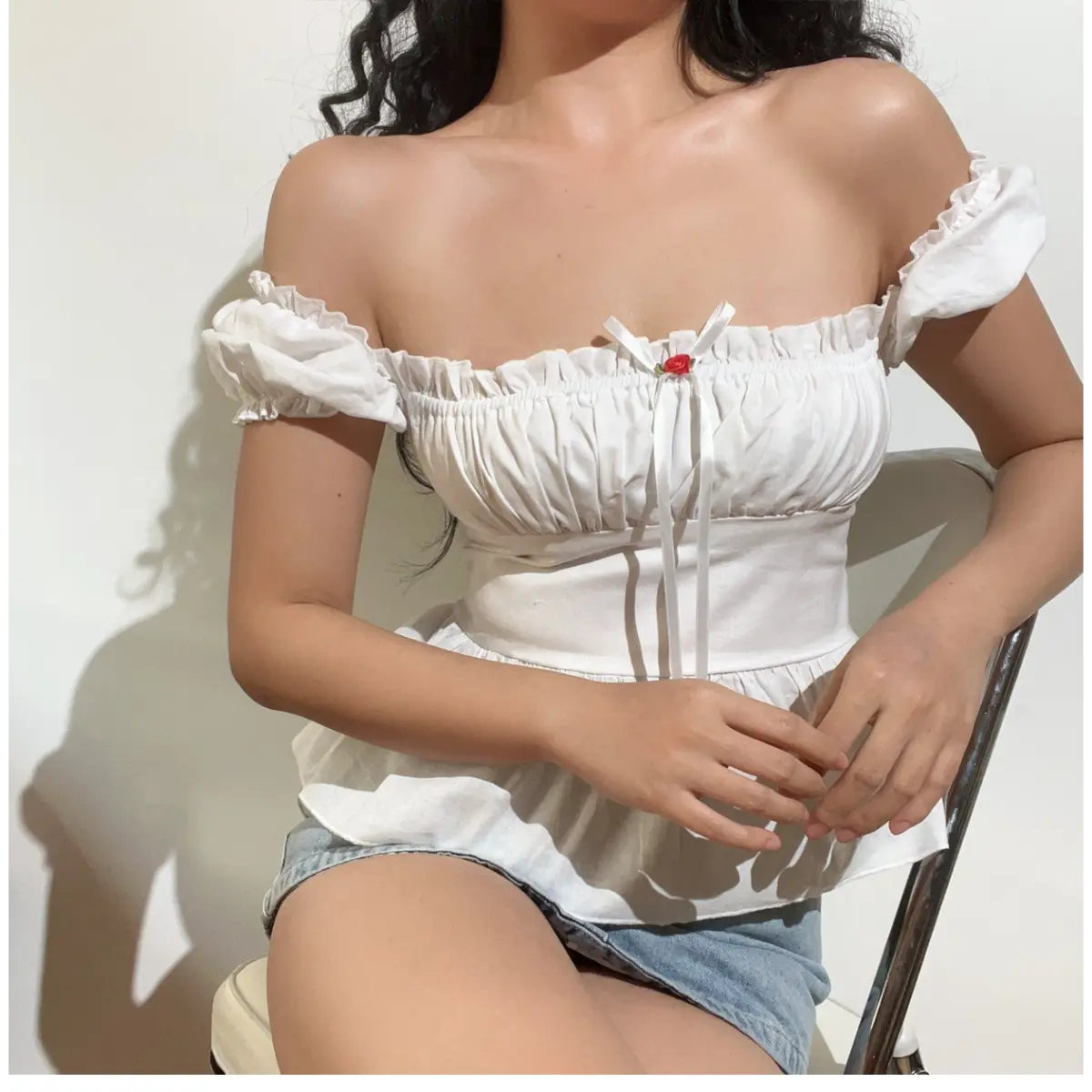 Seated view of a white off-shoulder peplum top, showcasing the puff sleeves, gathered bust, and flowy peplum hem.