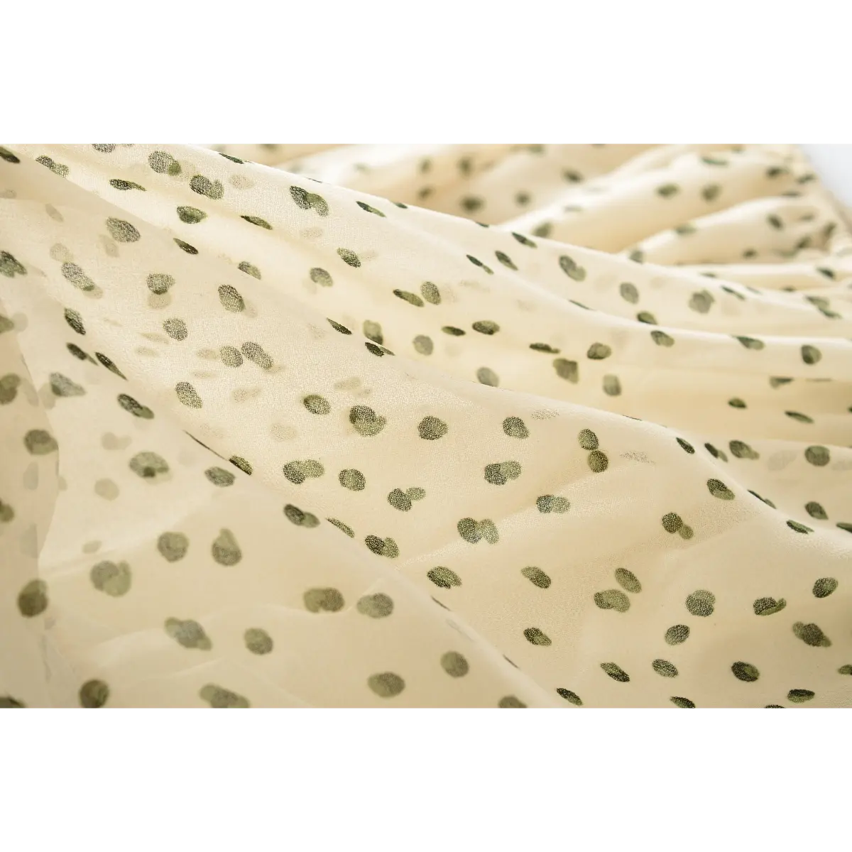Close-up of the sheer fabric on the off-shoulder cream blouse with green polka dots, showing the print texture and lightweight drape