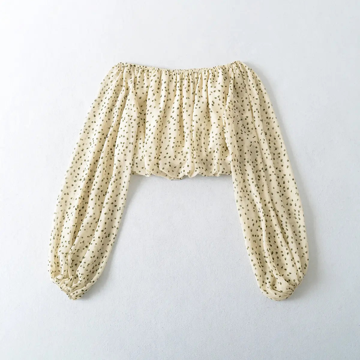 Flat-lay view of the off-shoulder cream blouse with green polka dots, showing the full silhouette and balloon sleeves