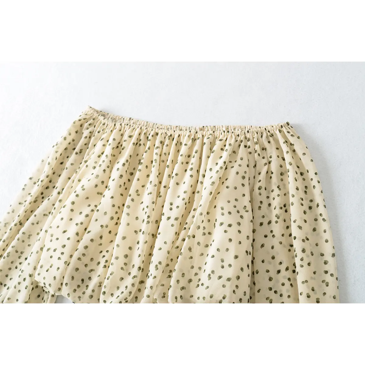 Side view of the gathered top elastic on the off-shoulder cream blouse with green polka dots, showing the stretch and fabric drape