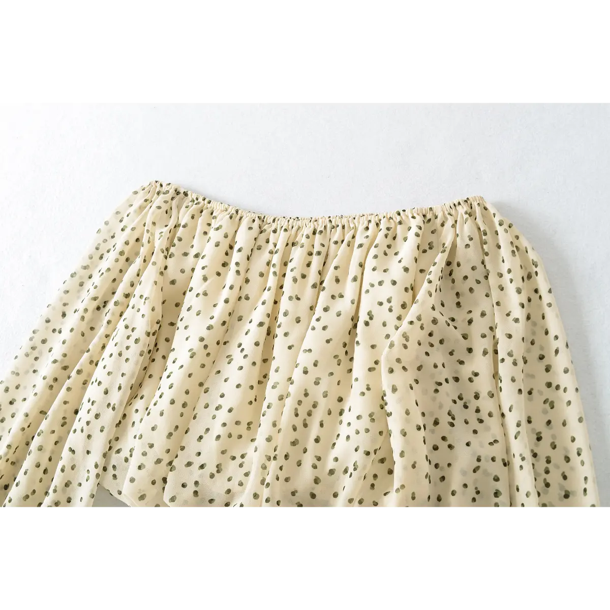 Close-up of the gathered top elastic on the off-shoulder cream blouse with green polka dots, showing the stretch and fabric drape