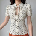 Lifestyle model wearing off white polka dot blouse, tie v neck, front bust ruched detail, puff short sleeve, tailored slim waist fit