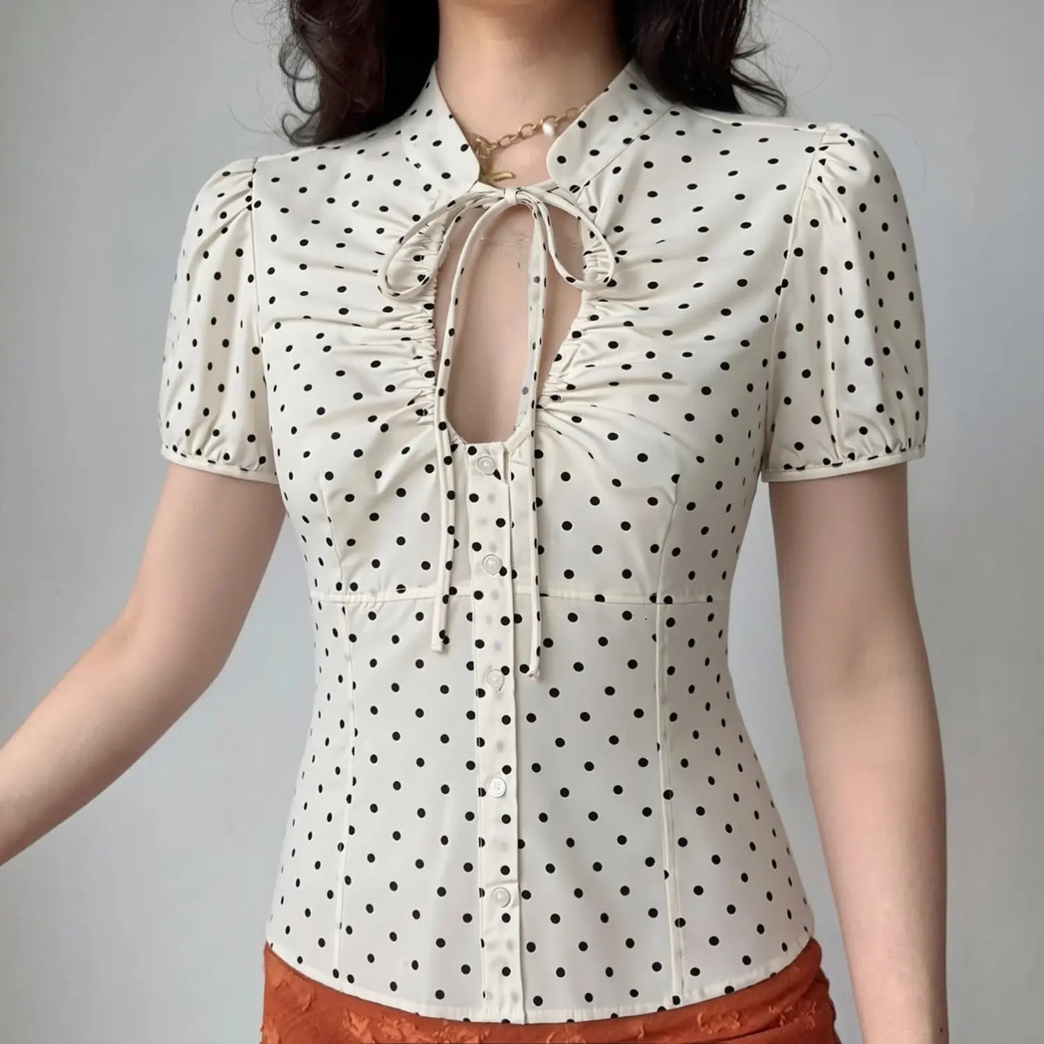 Lifestyle model wearing off white polka dot blouse, tie v neck, front bust ruched detail, puff short sleeve, tailored slim waist fit