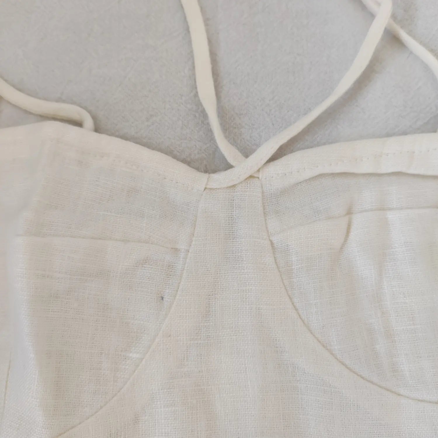 Close‑up bust seam, neckline stitching and tie strap detail off white linen cami top