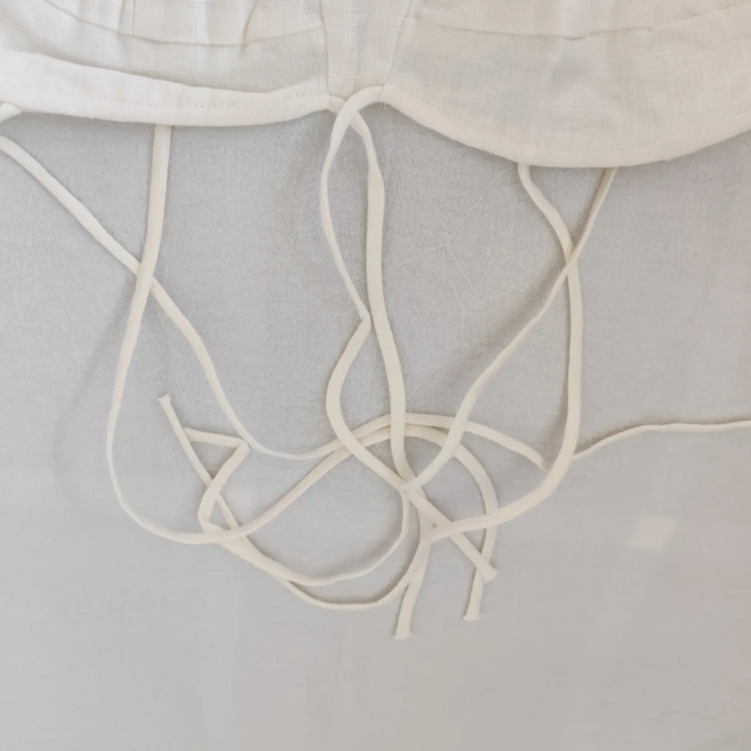 Close‑up loose tie spaghetti straps fabric detail off white linen camisole top