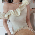 Women off white textured knit one shoulder crop top, 3d chiffon ruffle fitted waist, low angle partial indoor model photo