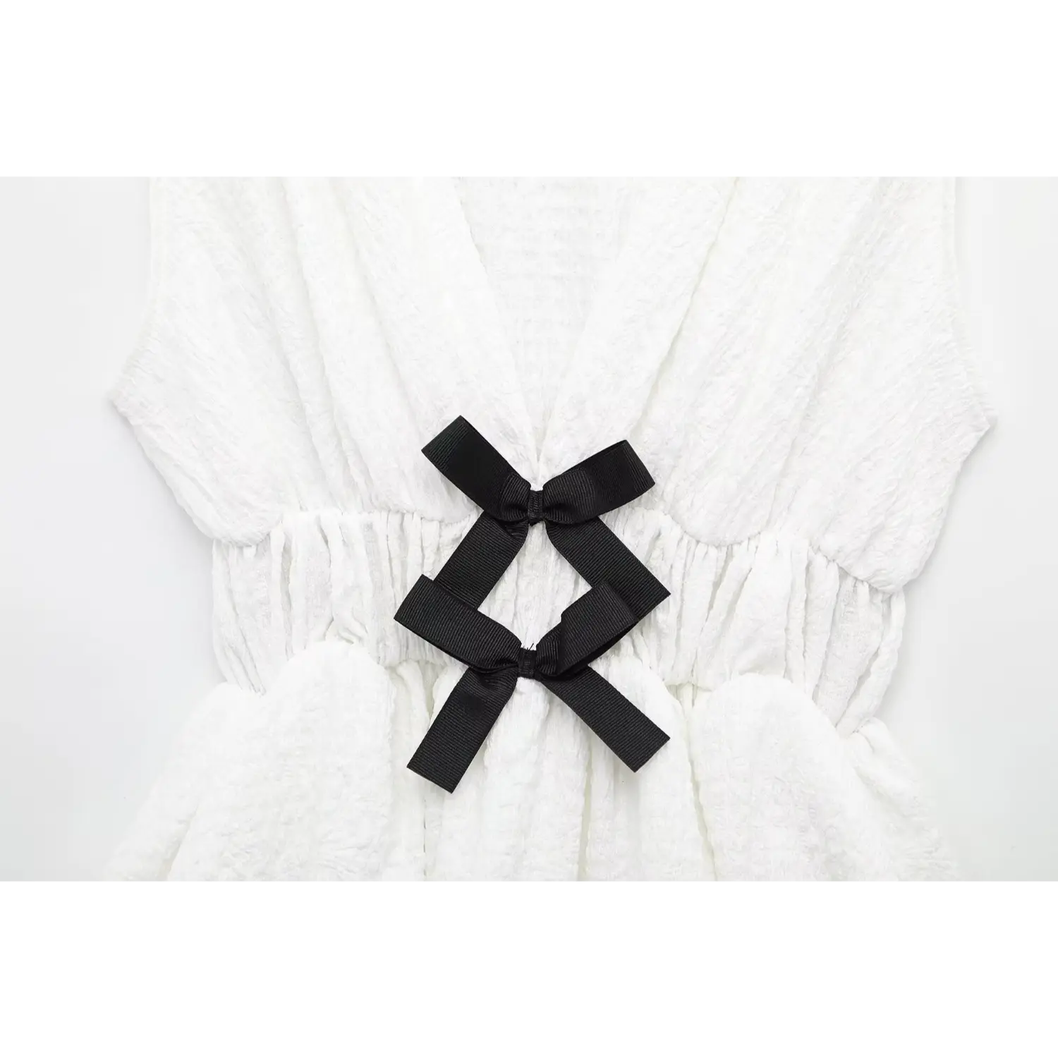 Close-up detail of black ribbon bows at the waist on off-white crinkled fabric peplum top