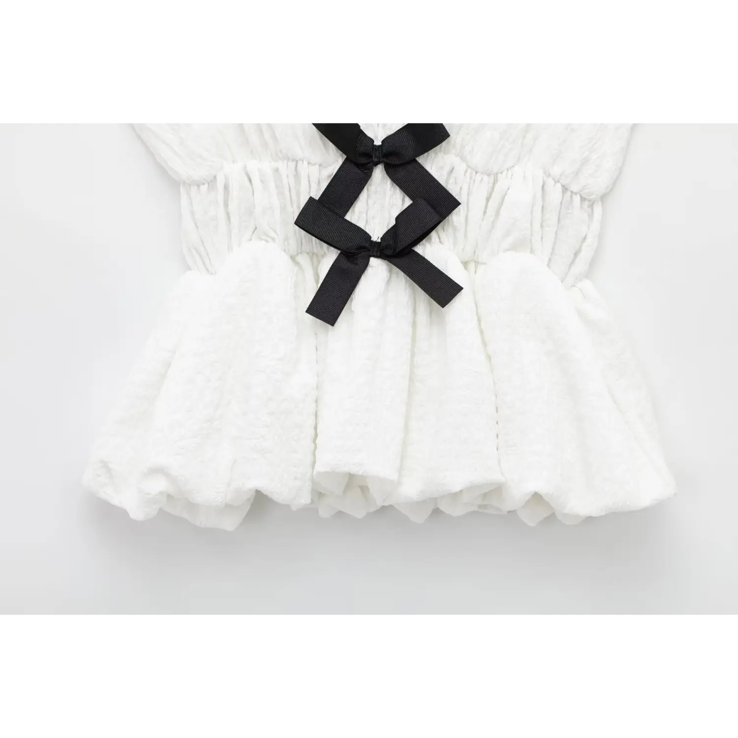 Close-up of flared peplum hem on off-white crinkled fabric sleeveless top