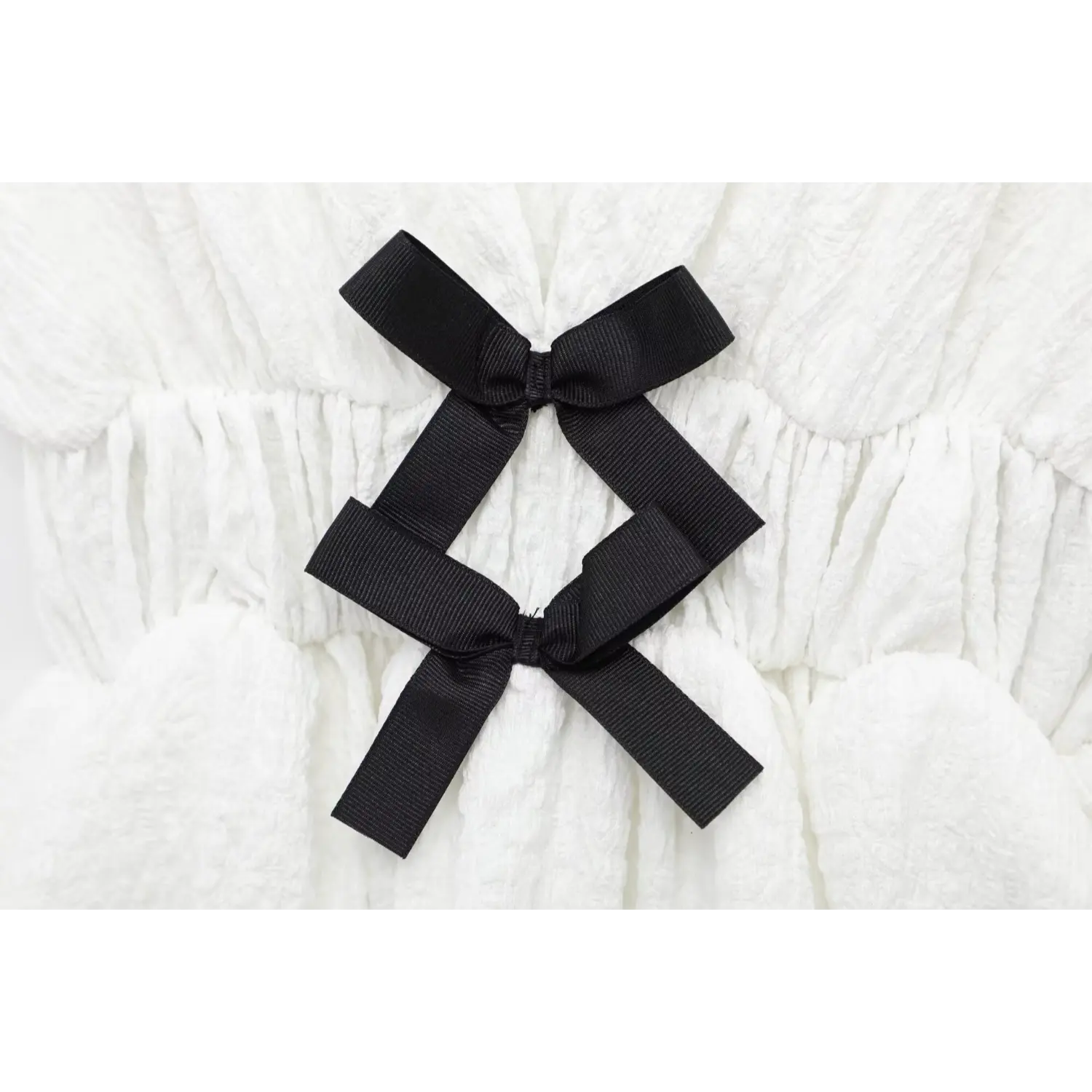 Macro shot of two black ribbon bows at the waist on off-white crinkled bubble fabric top