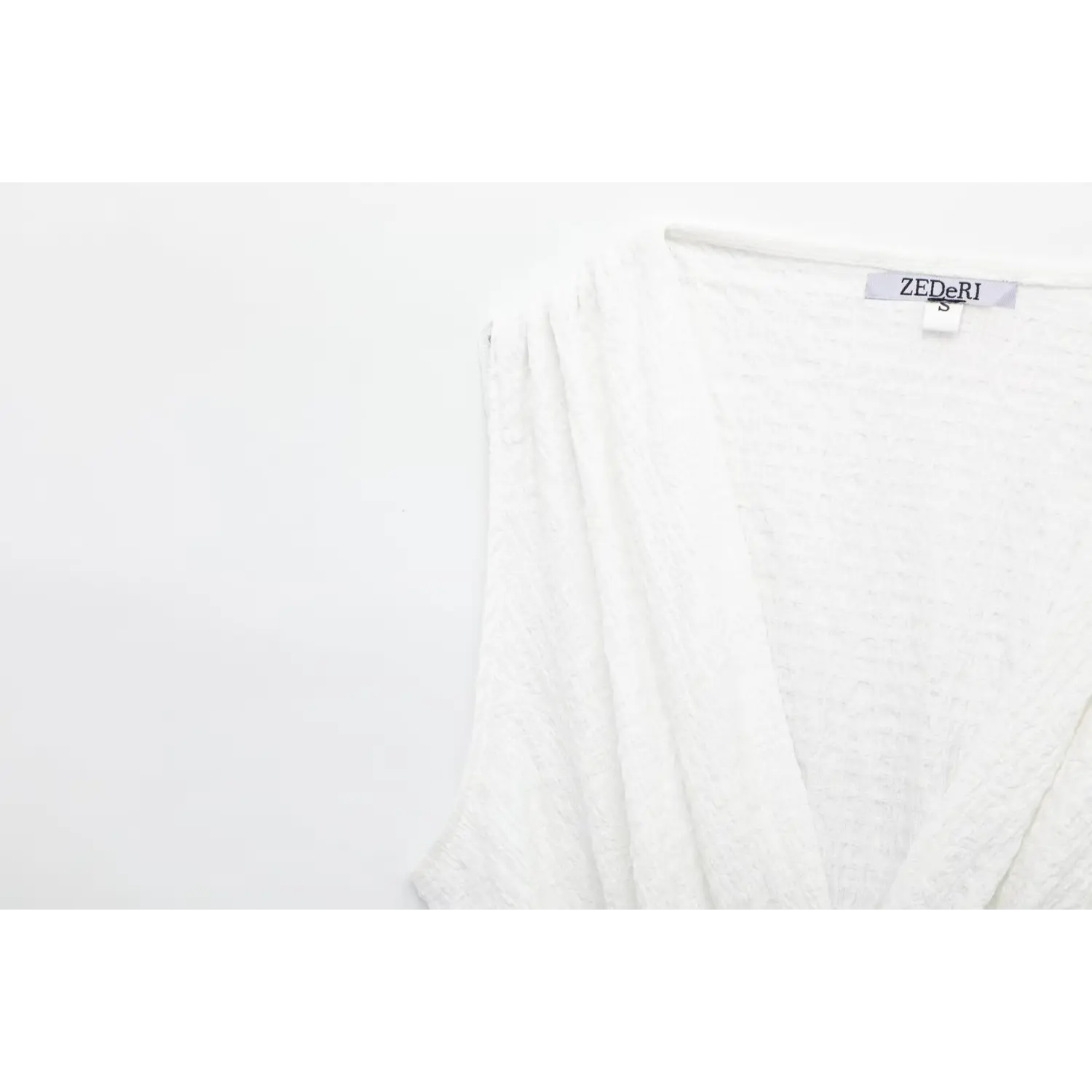 Close-up of inner neck label and V-neck seam detail on off-white sleeveless peplum top