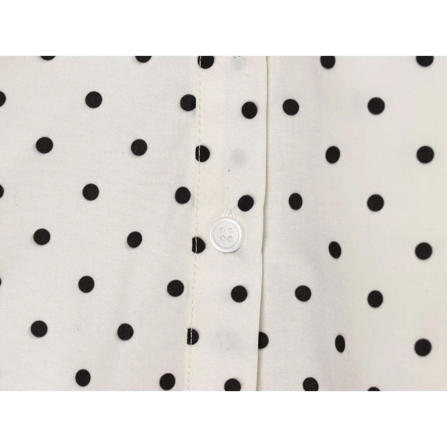 Closeup white round four-hole front button, matching off-white polka dot textile