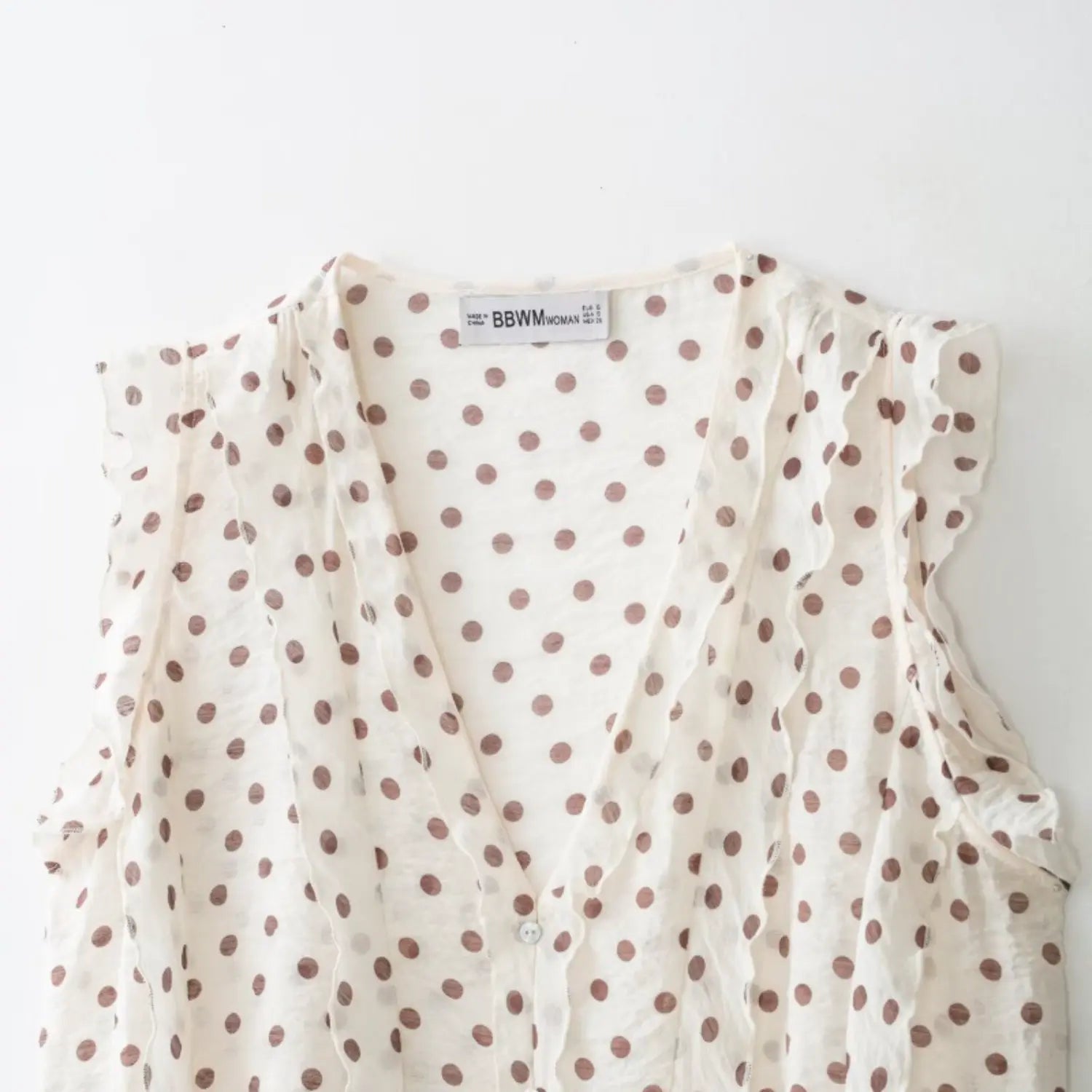 Full front neck shot, deep V neck, continuous wavy ruffles along placket and armholes, round shell buttons