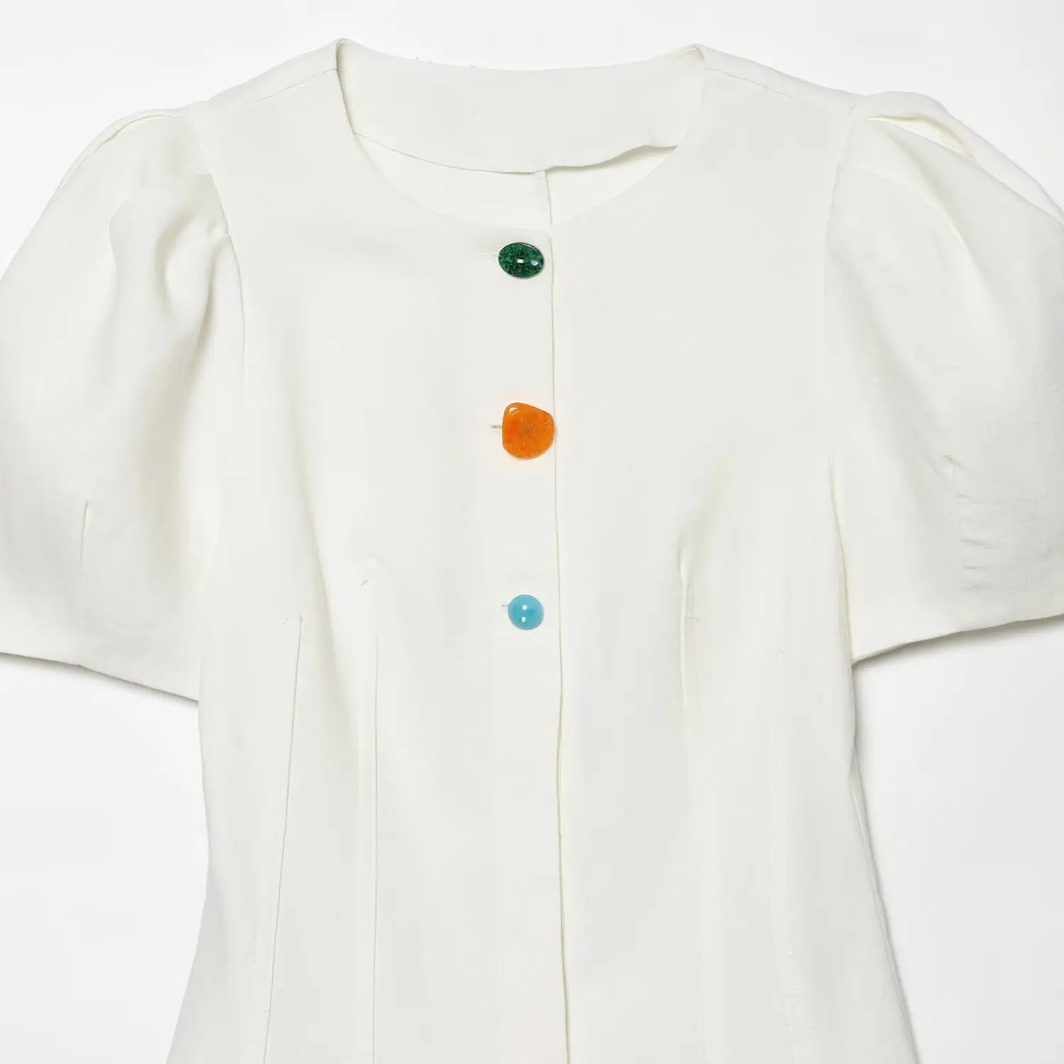 Close-up of the front placket with green, orange, and blue decorative buttons on the off-white dress