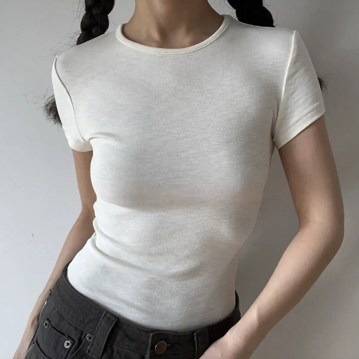 Lifestyle shot of form-fitting off-white ribbed crew-neck short-sleeve t-shirt, tucked into jeans