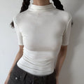 Lifestyle shot of form-fitting off-white ribbed half-turtleneck short-sleeve top, tucked into jeans