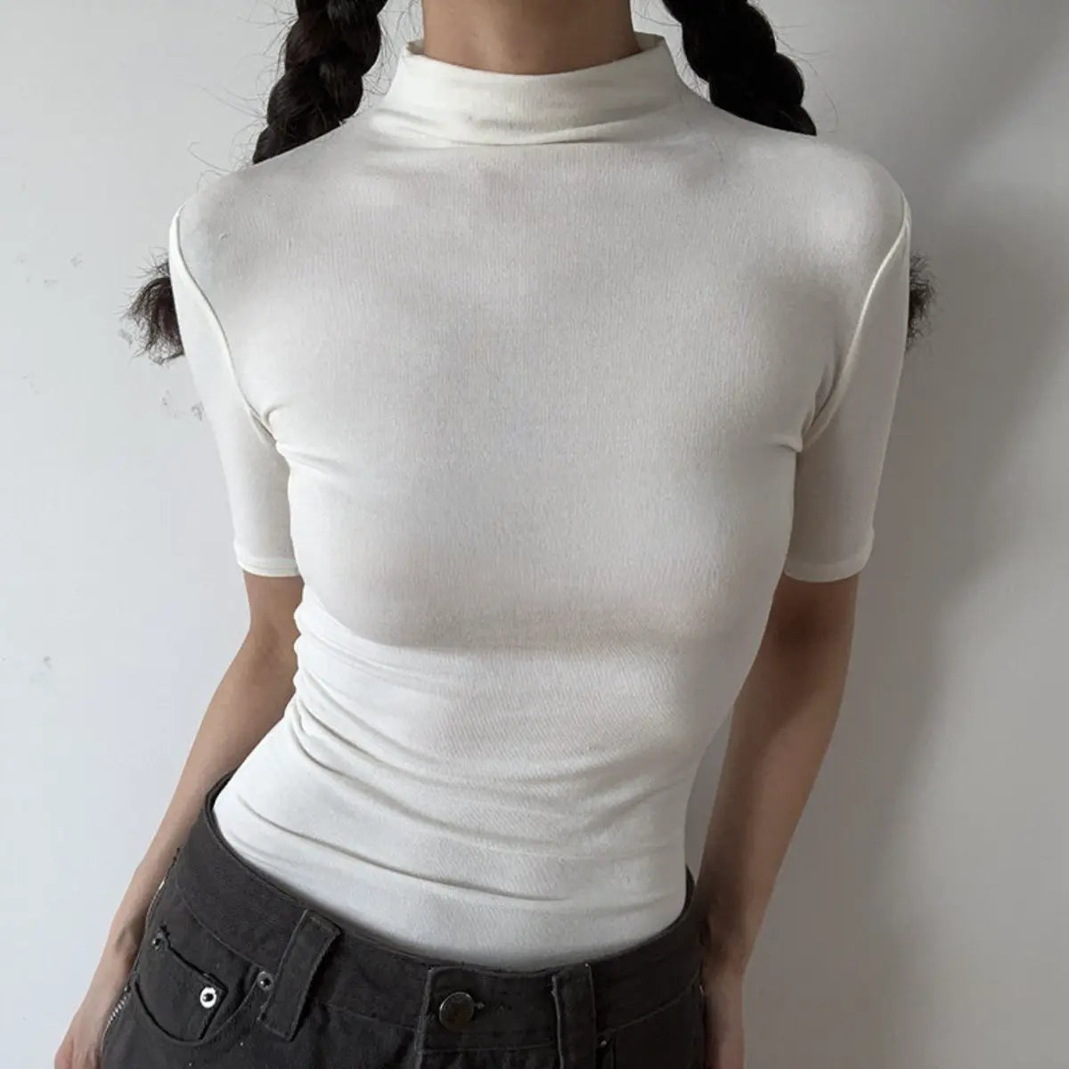 Lifestyle shot of form-fitting off-white ribbed half-turtleneck short-sleeve top, tucked into jeans