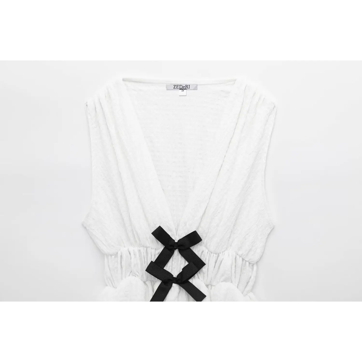 Full front view of off-white crinkled fabric peplum top with V-neck, black bows, and inner label visible