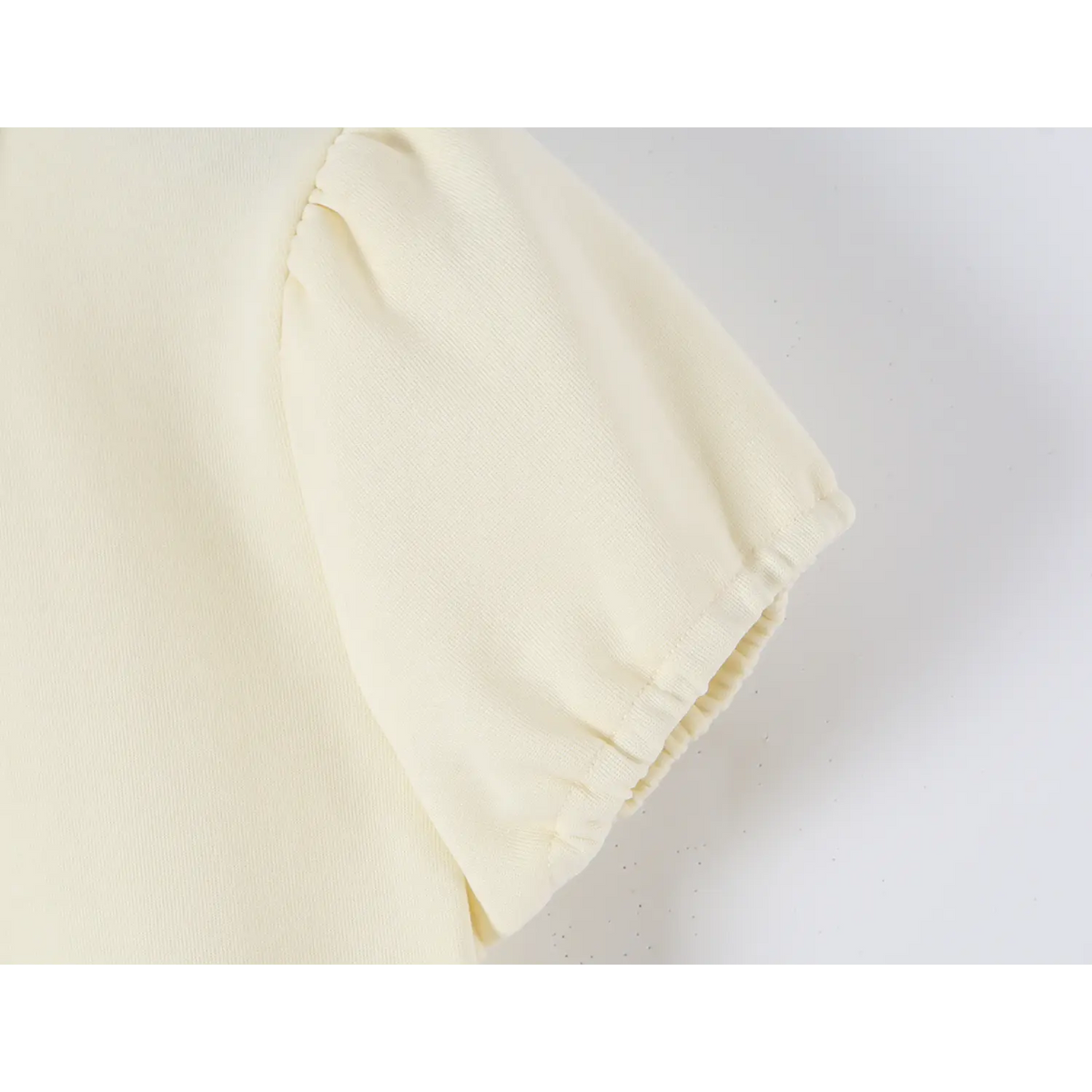Close-up of offwhite dress puff short sleeve, elasticated cuff and fine knit fabric texture