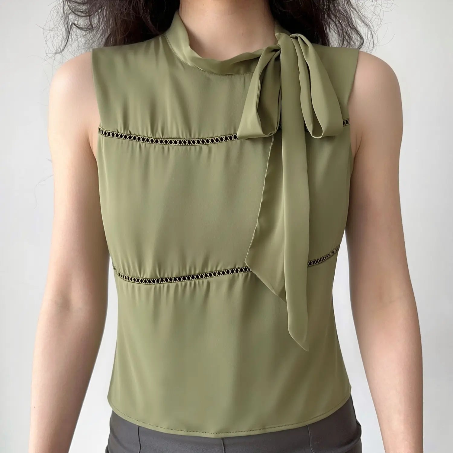 Lifestyle model shot olive green satin sleeveless top, stand neck side bow tie, diagonal hollow ladder cutout panels, tailored slim silhouette
