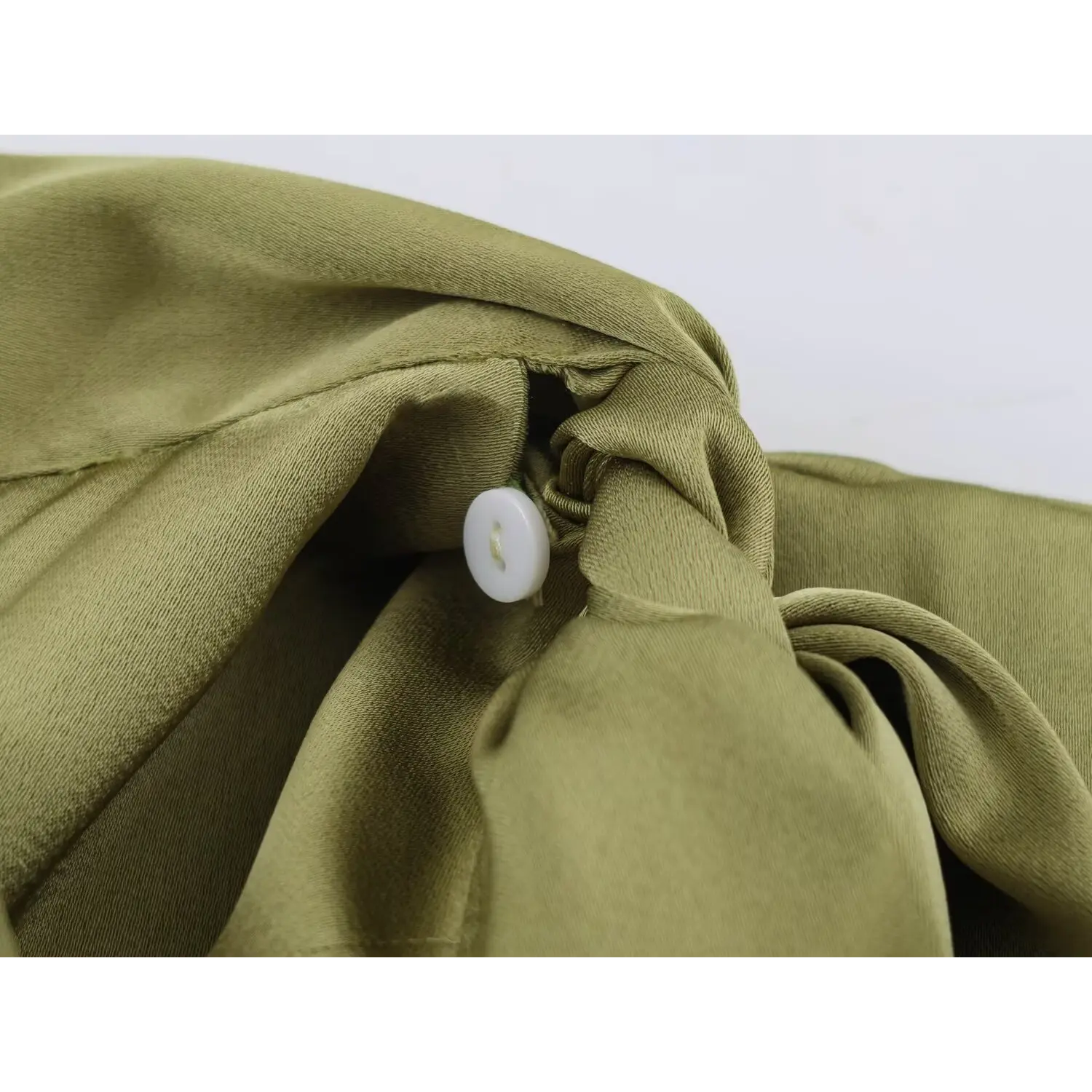 Closeup hidden white round button at neck tie knot, olive green silky satin sleeveless blouse inner fastening detail