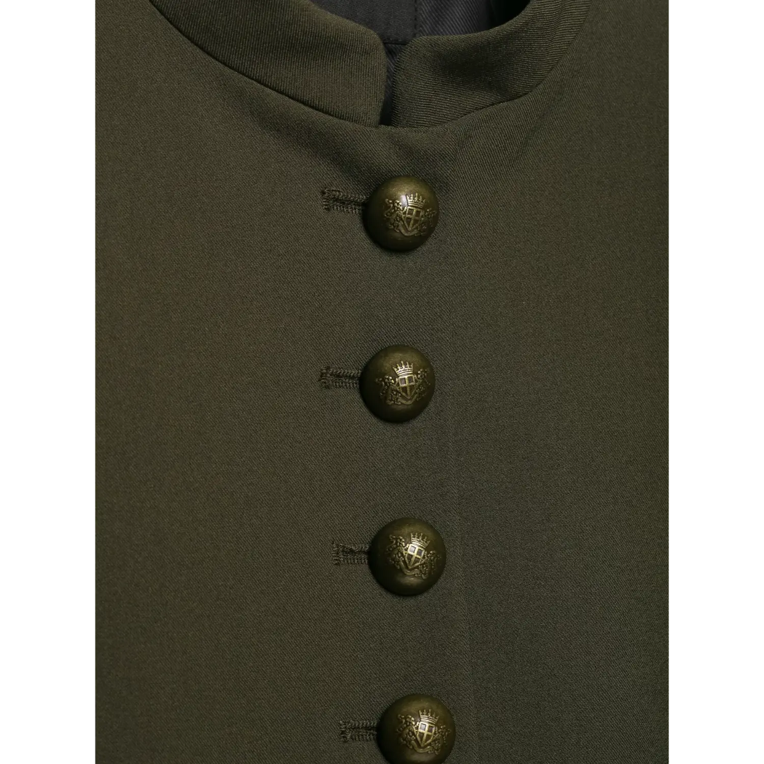 Extreme close‑up of vintage embossed crest metal buttons on olive green cropped military blazer