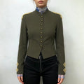 Model wearing olive green cropped military blazer, front view, paired with black pants, gold braid shoulder and cuff accents
