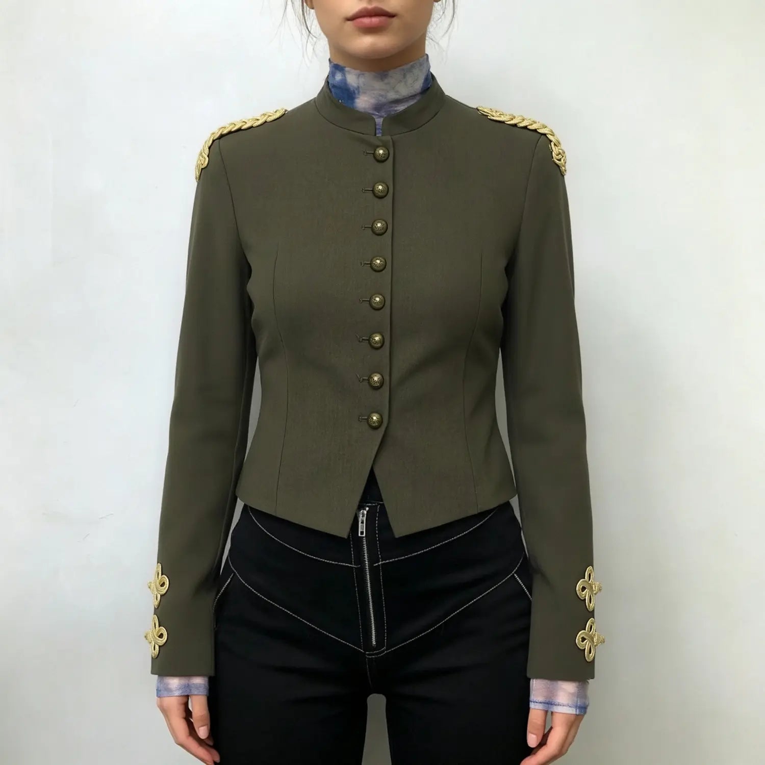 Model wearing olive green cropped military blazer, front view, paired with black pants, gold braid shoulder and cuff accents