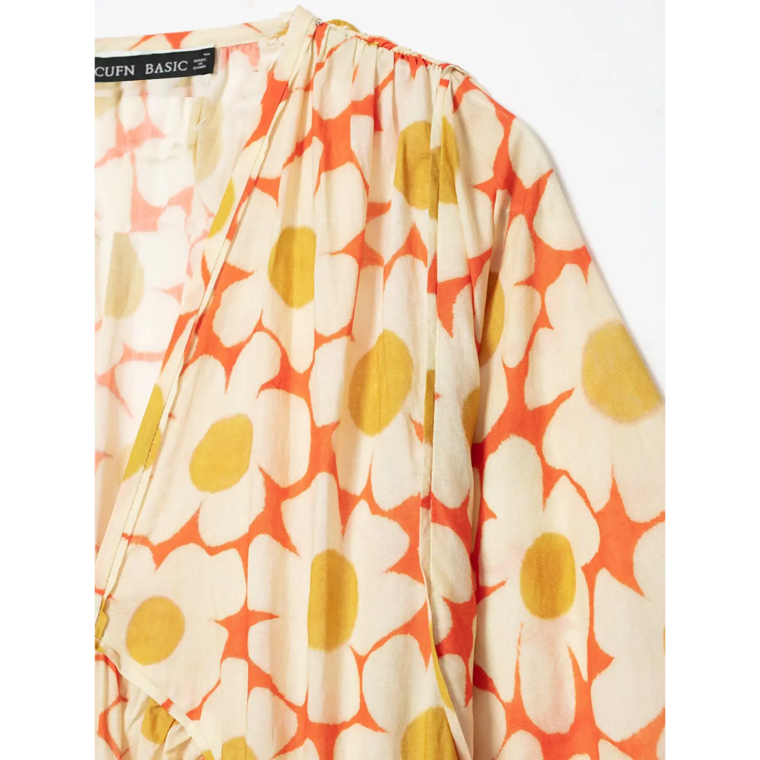 Close‑up view of neck label and gathered shoulder on orange daisy floral print maxi dress