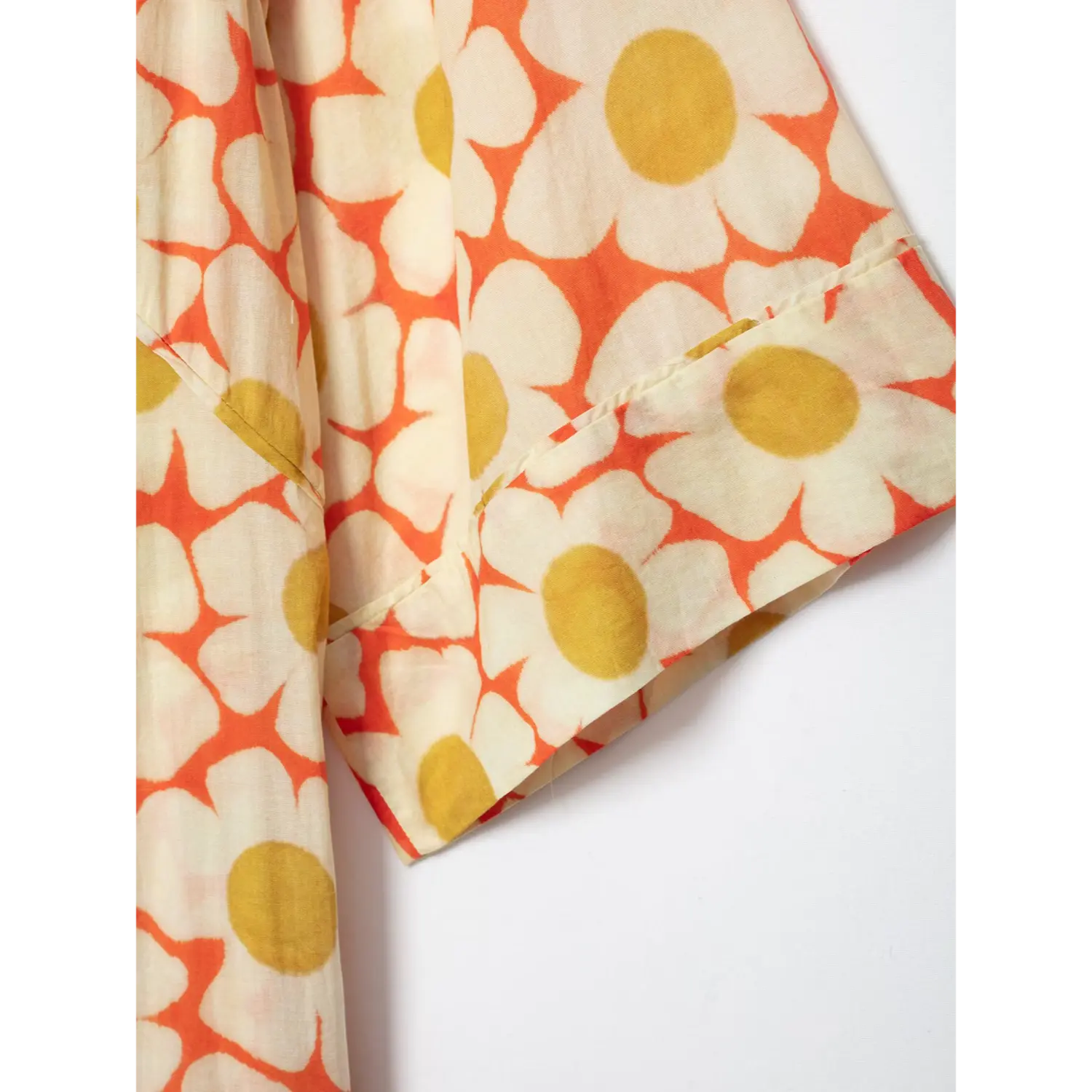 Close‑up of kimono sleeve cuff seam on orange daisy floral maxi dress