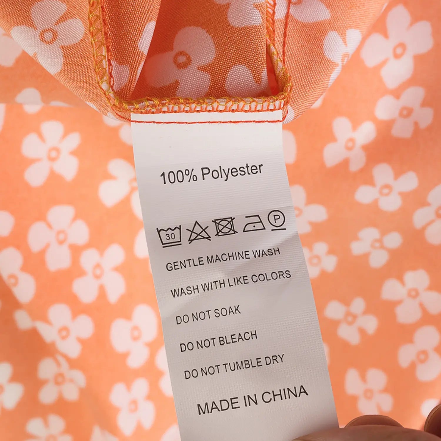 Close-up of the care label on the orange floral dress, showing 100% polyester composition and washing instructions