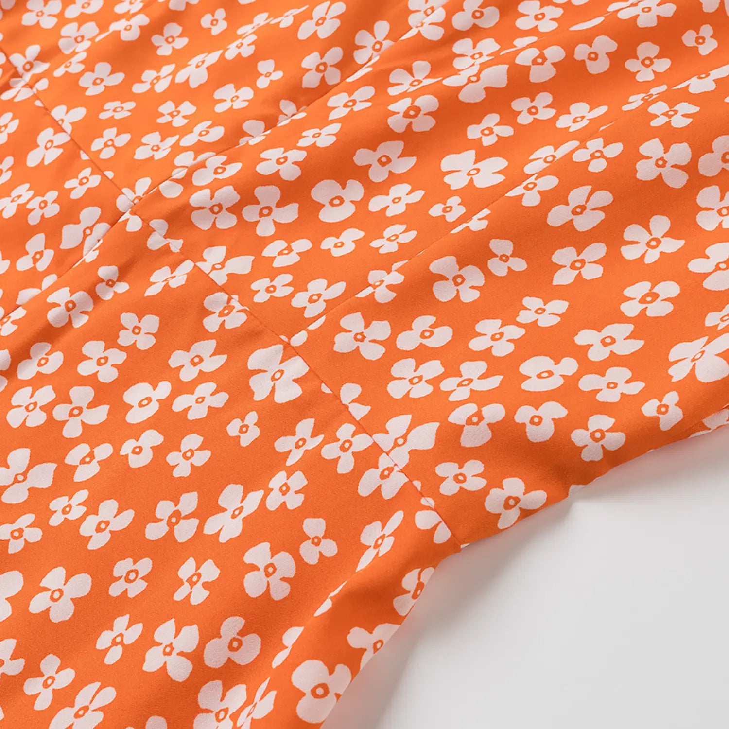 Close-up of the white floral print on the orange polyester fabric dress, showing the seam line