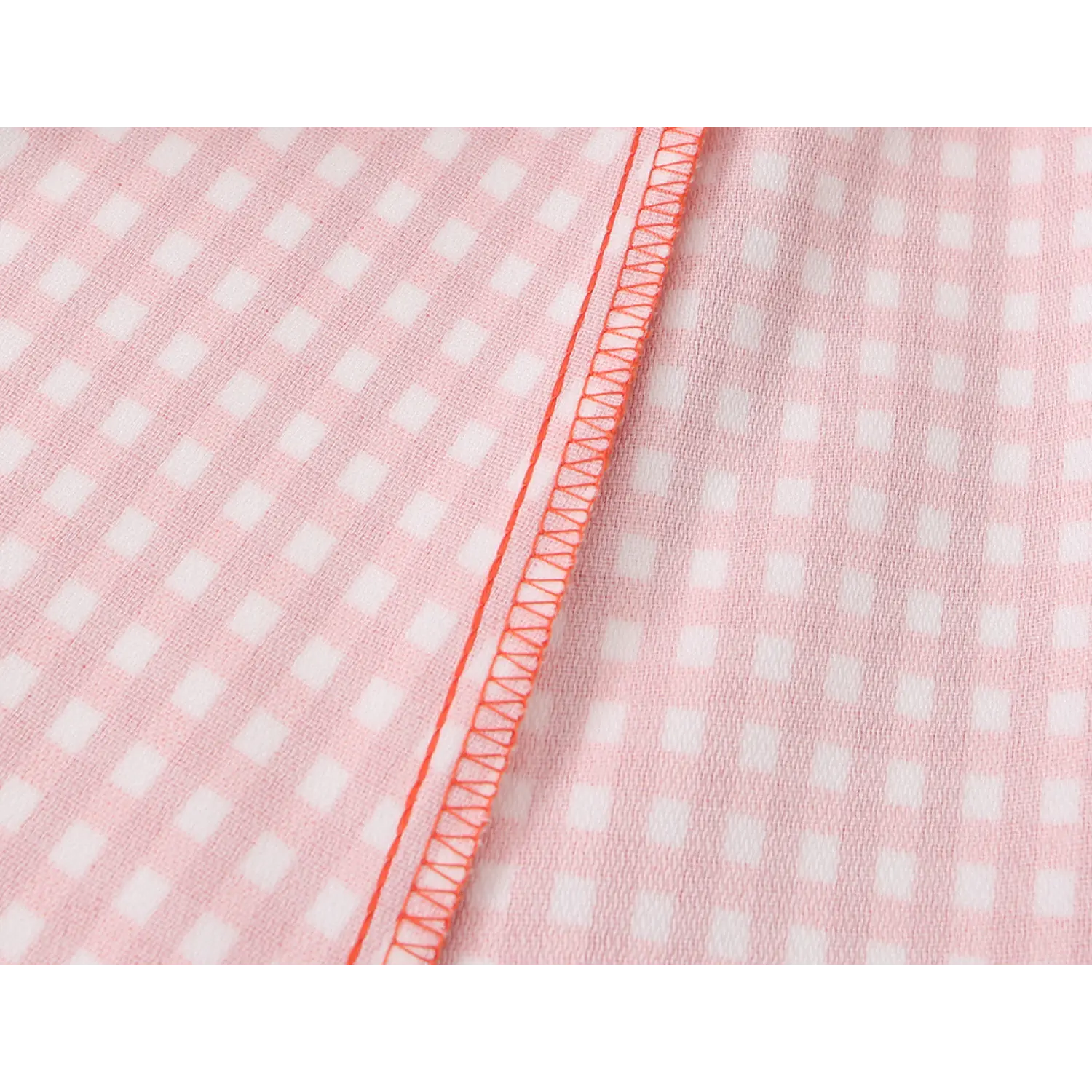 Macro shot of outer orange gingham fabric and pale pink inner lining, neat orange matching overlock stitching along seam edge
