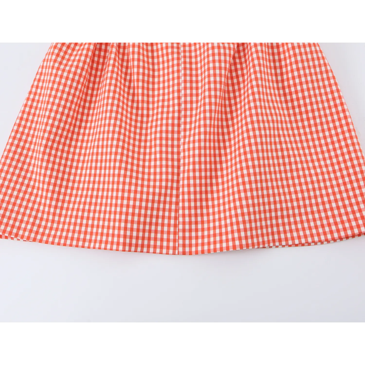 Flat full skirt close-up, waist gathered pleats forming flared A-line mini hem, uniform small orange gingham check print