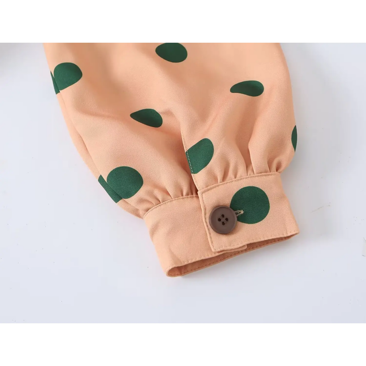 Cuff closeup of orange green polka dot trench coat, button decorated long sleeve cuff