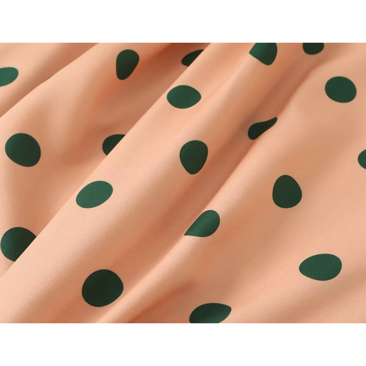 Fabric close up of women orange trench coat with large green polka dot print, smooth lightweight material