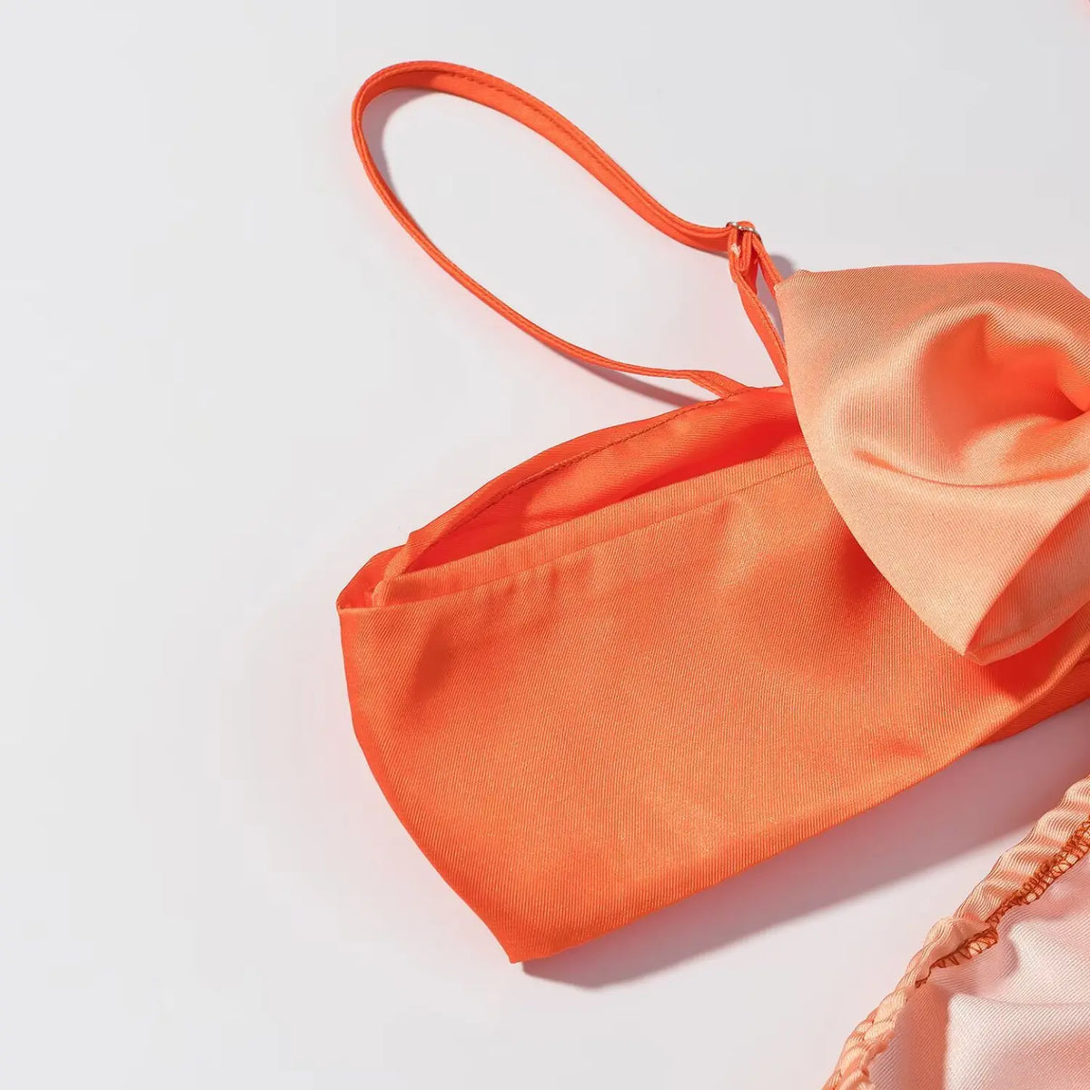 Close-up of orange satin maxi dress bust cup with adjustable thin spaghetti strap, smooth glossy orange satin fabric