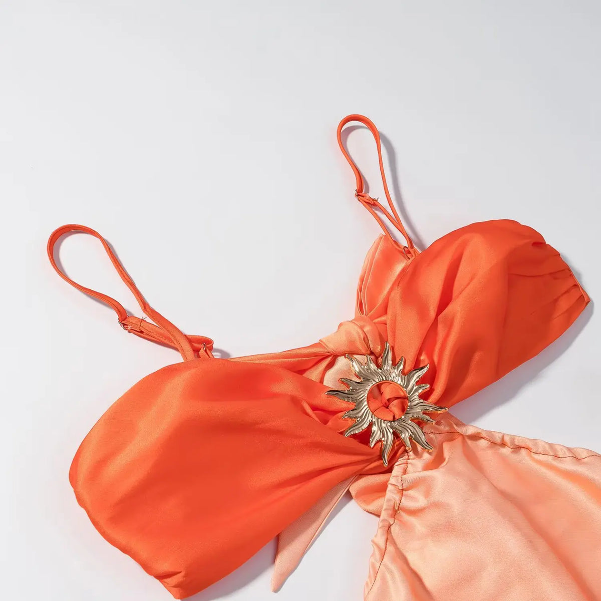 Flat lay close-up of orange satin maxi dress bust part, adjustable thin spaghetti straps and metallic sun shape decor on knotted fabric