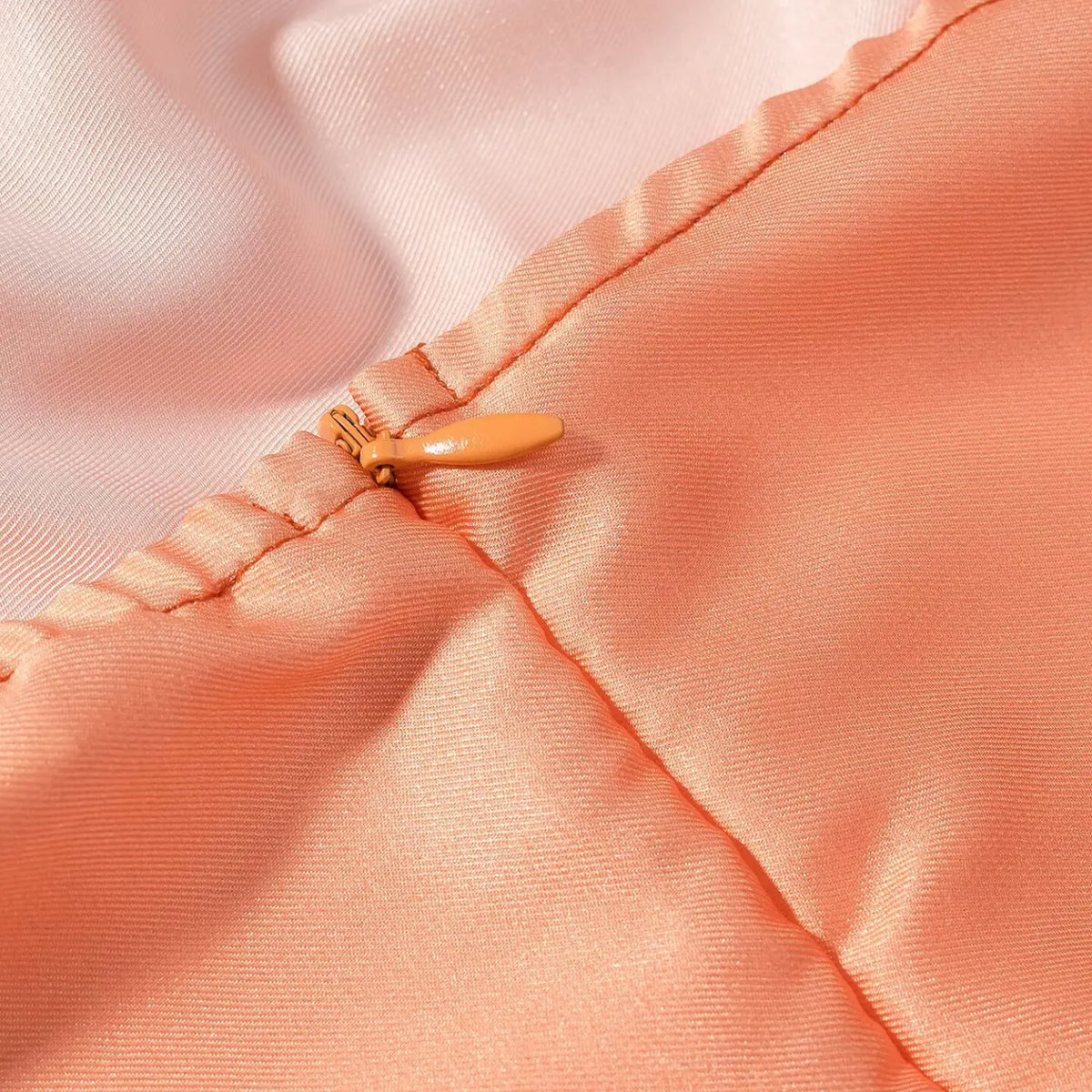 Macro close-up of orange hidden side zipper on satin maxi dress, matching orange zipper pull on glossy skirt fabric