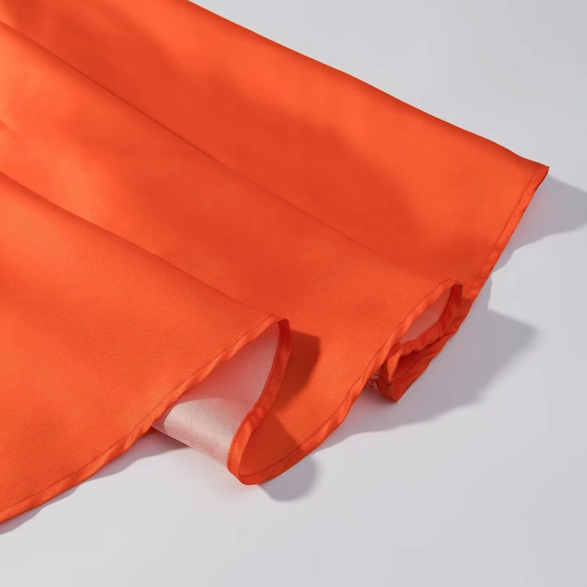 Close-up of orange satin maxi dress skirt hem, neat finished edge with inner lining visible