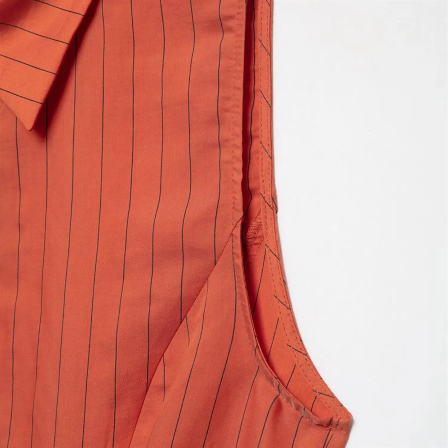 Sleeveless armhole inner binding close-up, neat folded edge stitching, side panel seam, lightweight orange stripe fabric