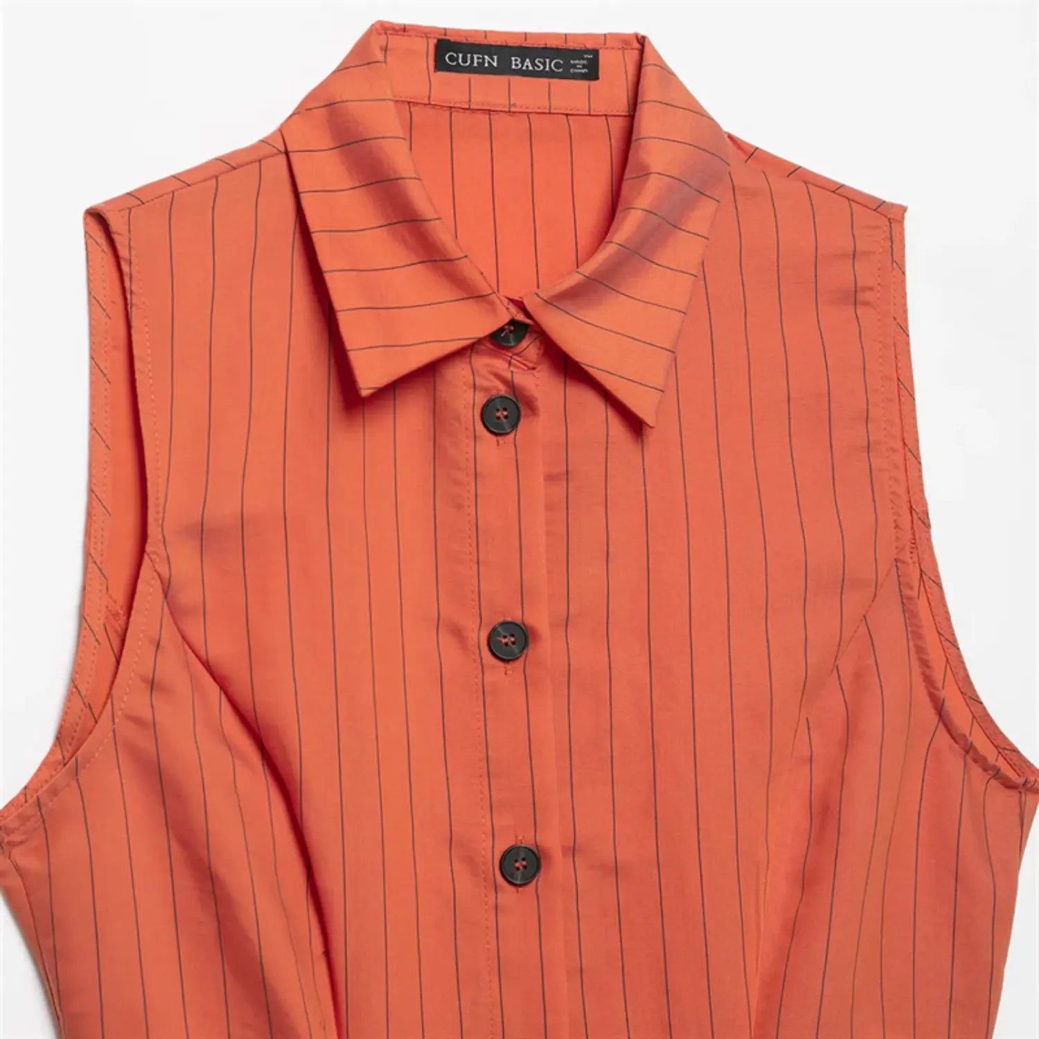 Front upper detail of orange sleeveless blouse, pointed turn-down collar, vertical thin black stripes, front button placket, dark round buttons, smooth lightweight woven fabric
