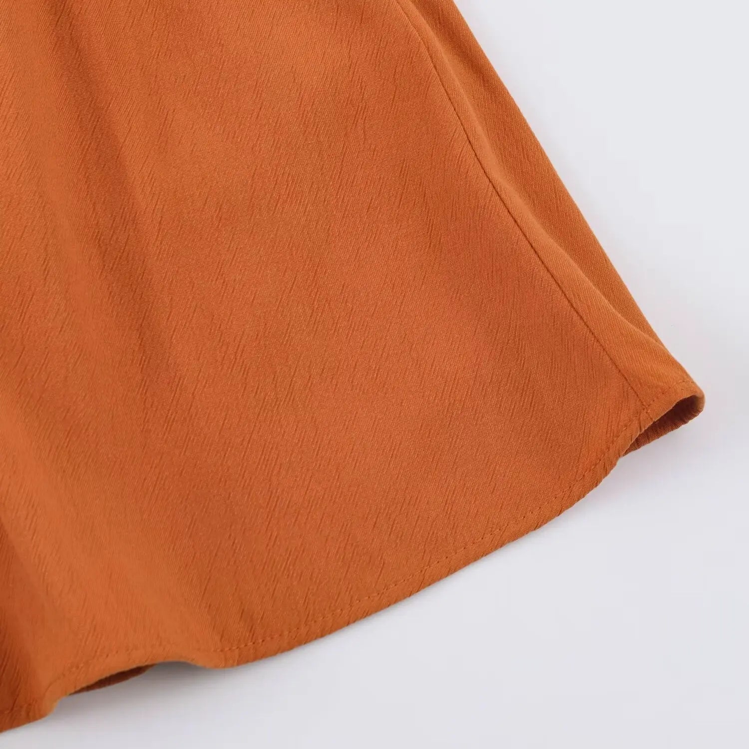 Close-up of short leg hem edge on rust sleeveless romper, neat finished stitching on textured woven fabric