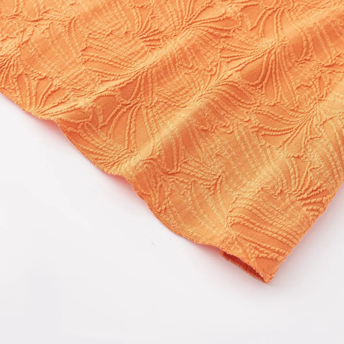 Close-up shot of orange embossed leaf fabric, showing the raised texture and detailed leaf pattern.
