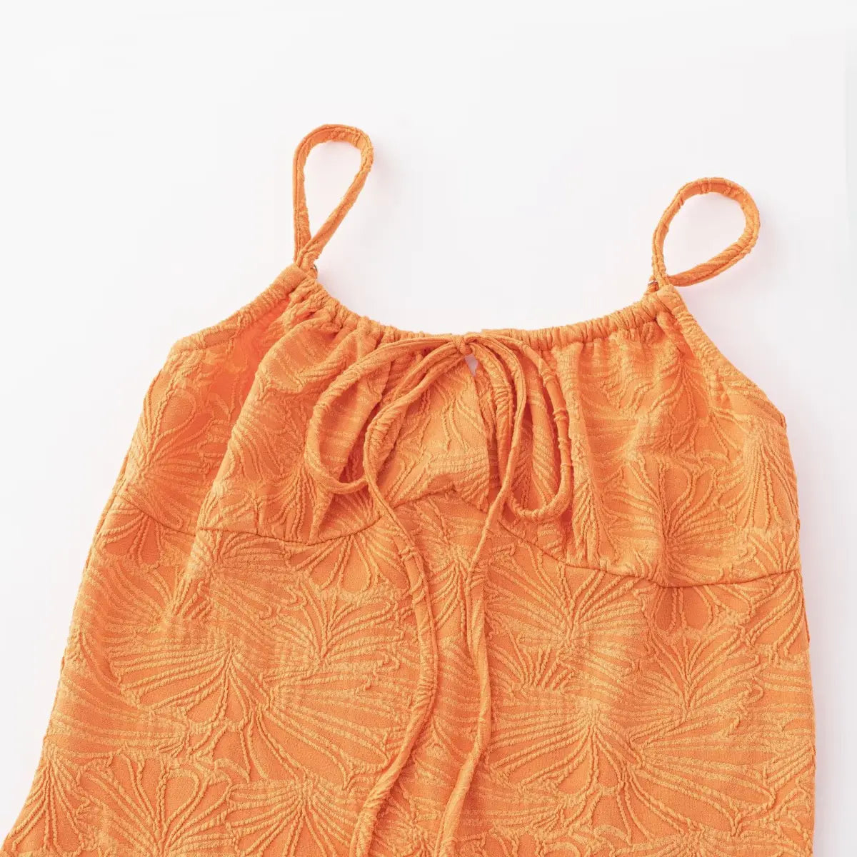 Close-up view of the bust area of an orange textured mini dress with spaghetti straps, showing the front tie keyhole detail and embossed leaf pattern.