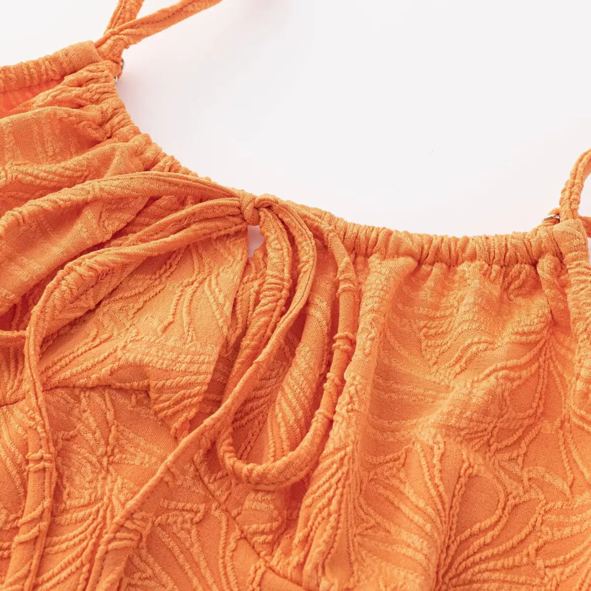 Macro view of the front tie keyhole detail on an orange textured mini dress, highlighting the embossed leaf fabric pattern.