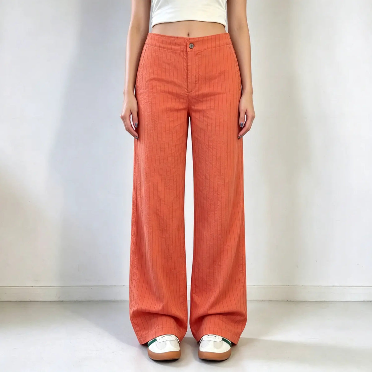 Model wearing orange thin stripe wide leg trousers, button zipper fly, textured lightweight fabric, relaxed wide leg cut, paired with white cropped top, plain white background