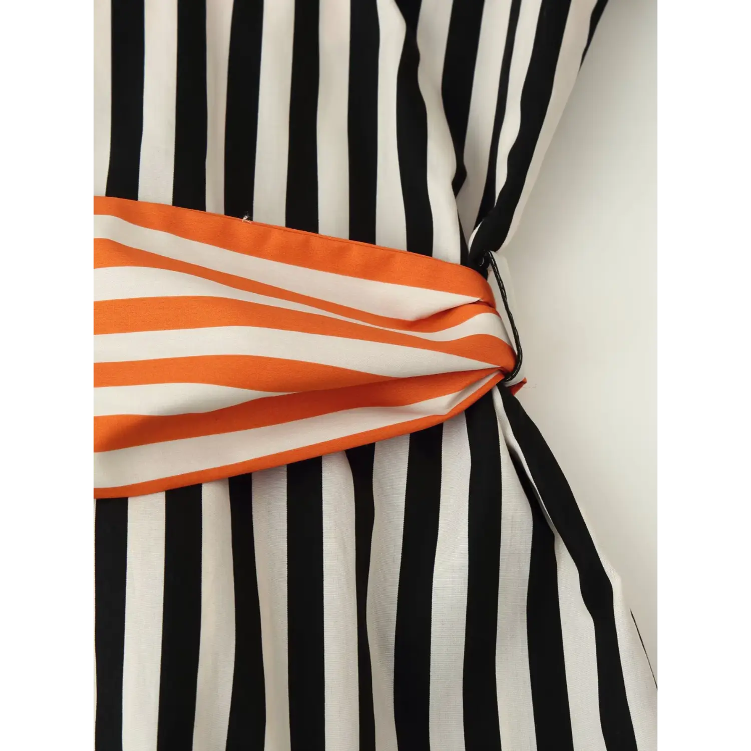 Close‑up of side seam where orange‑white striped sash attaches to black‑white striped shirt, fabric folding and stitching detail