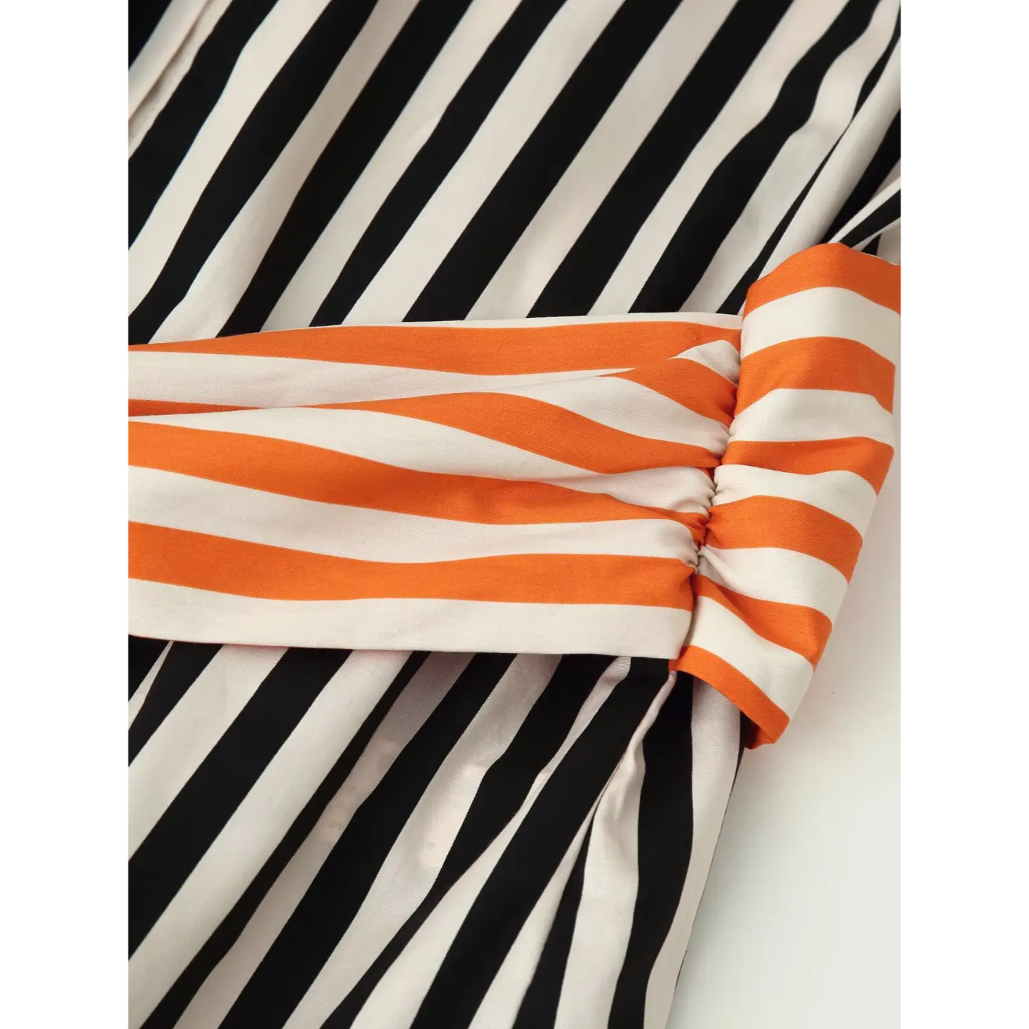 Close‑up of knotted orange‑white striped fabric sash belt wrapped around shirt waist, fabric fold and stitching detail